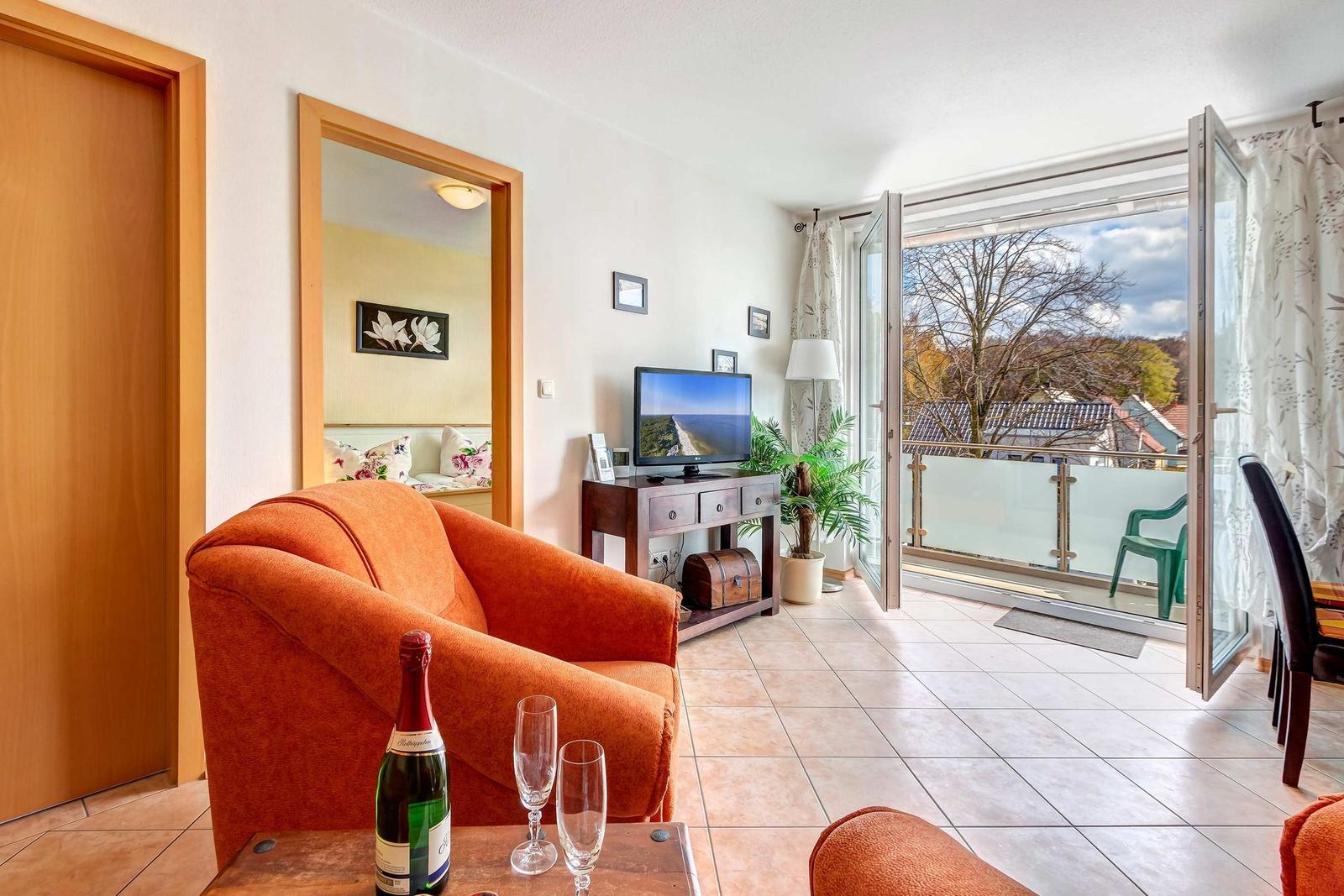 Wohnzimmer mit orangefarbenem Sofa, TV und Balkonansicht.