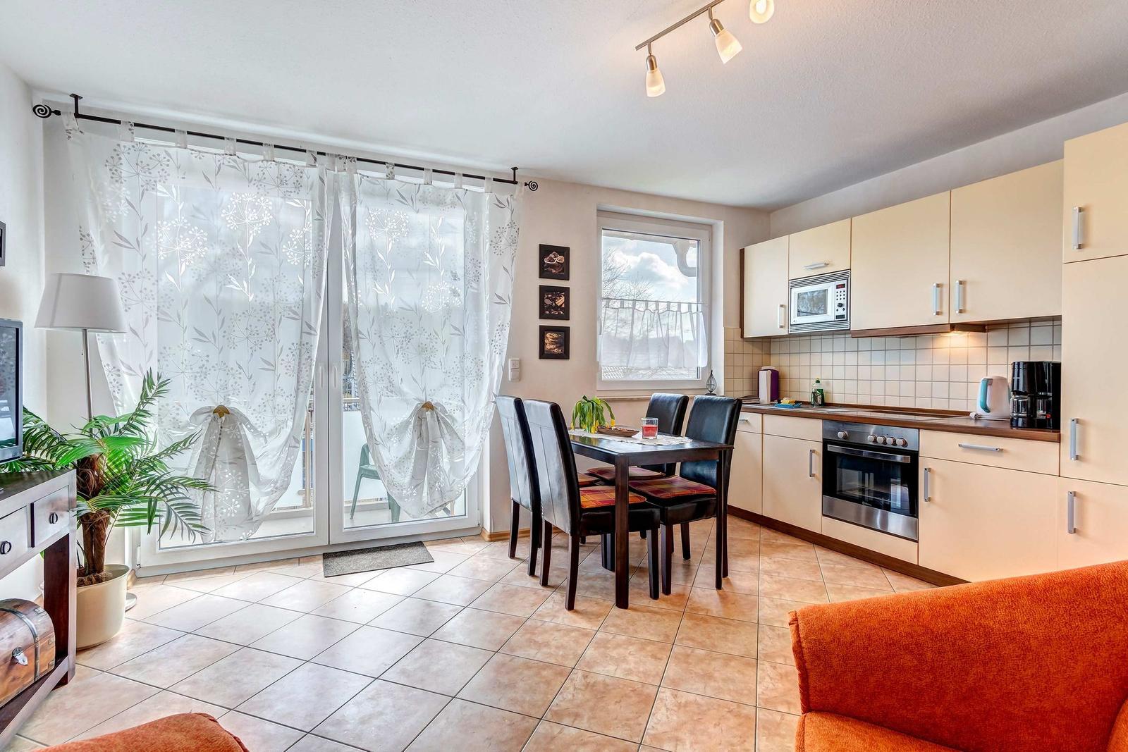 Küche und Essbereich mit Esszimmer, Fenster und Balkon. Wohnbereich mit Sofa und Pflanze.