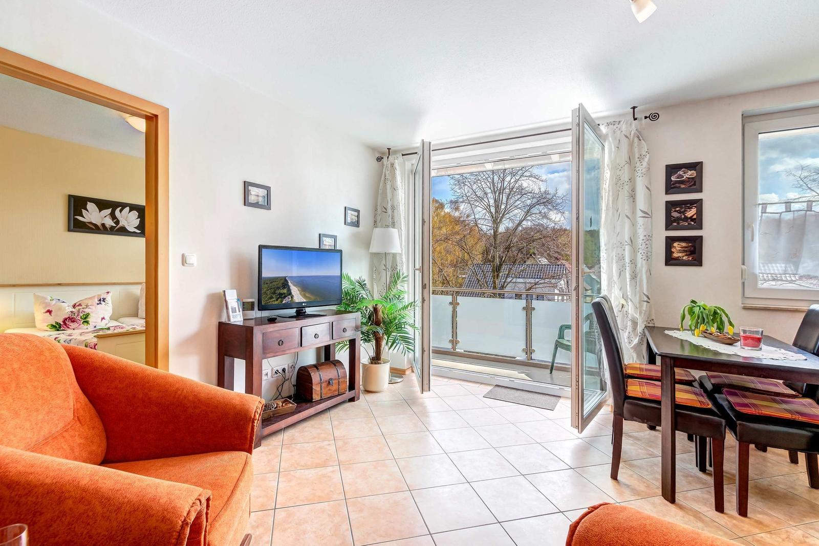 Wohn- und Essbereich mit Balkon, Fernseher und Schlafzimmer im Hintergrund.