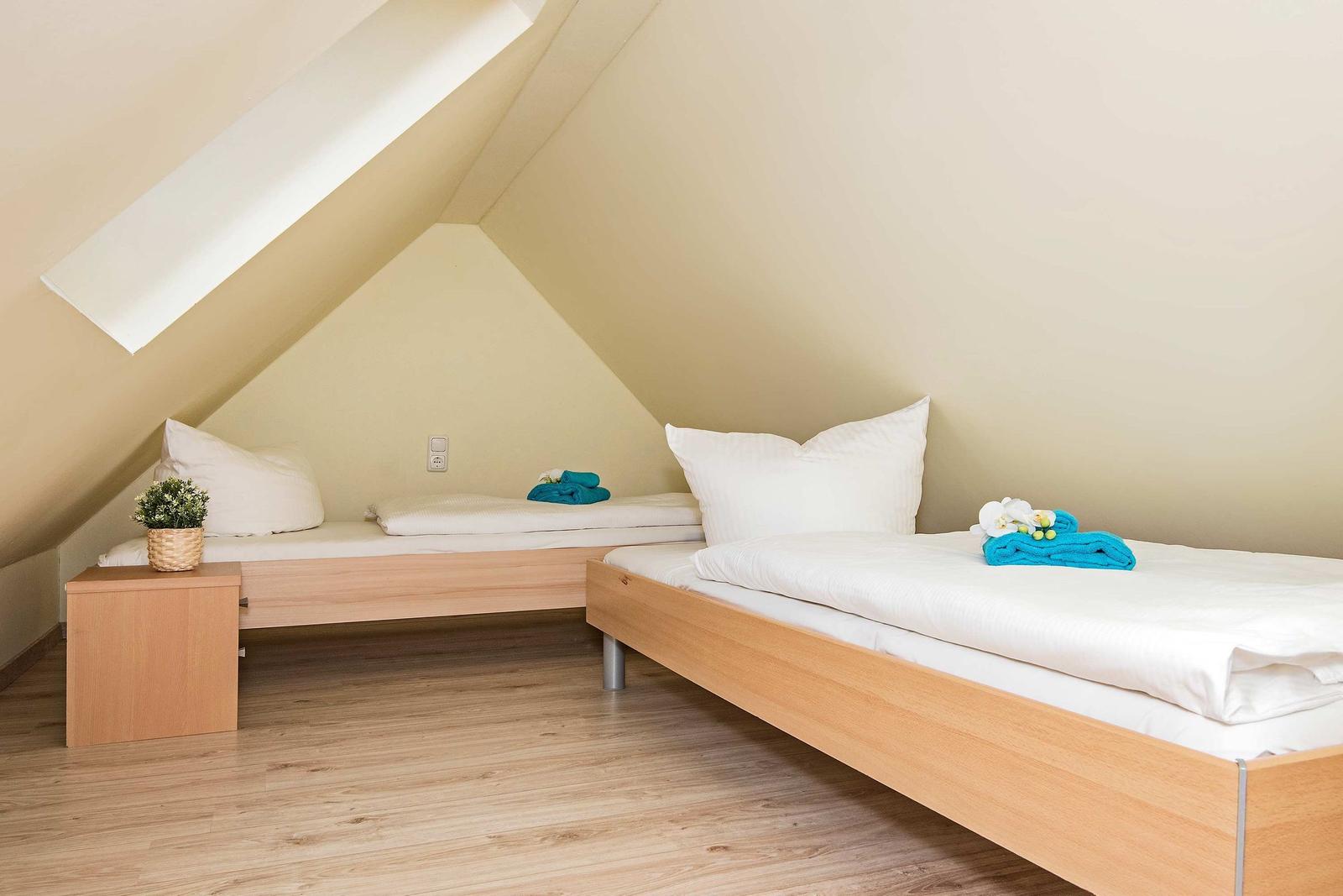 Zwei Betten unter Dachschrägen mit Holzgestell und weißer Bettwäsche.