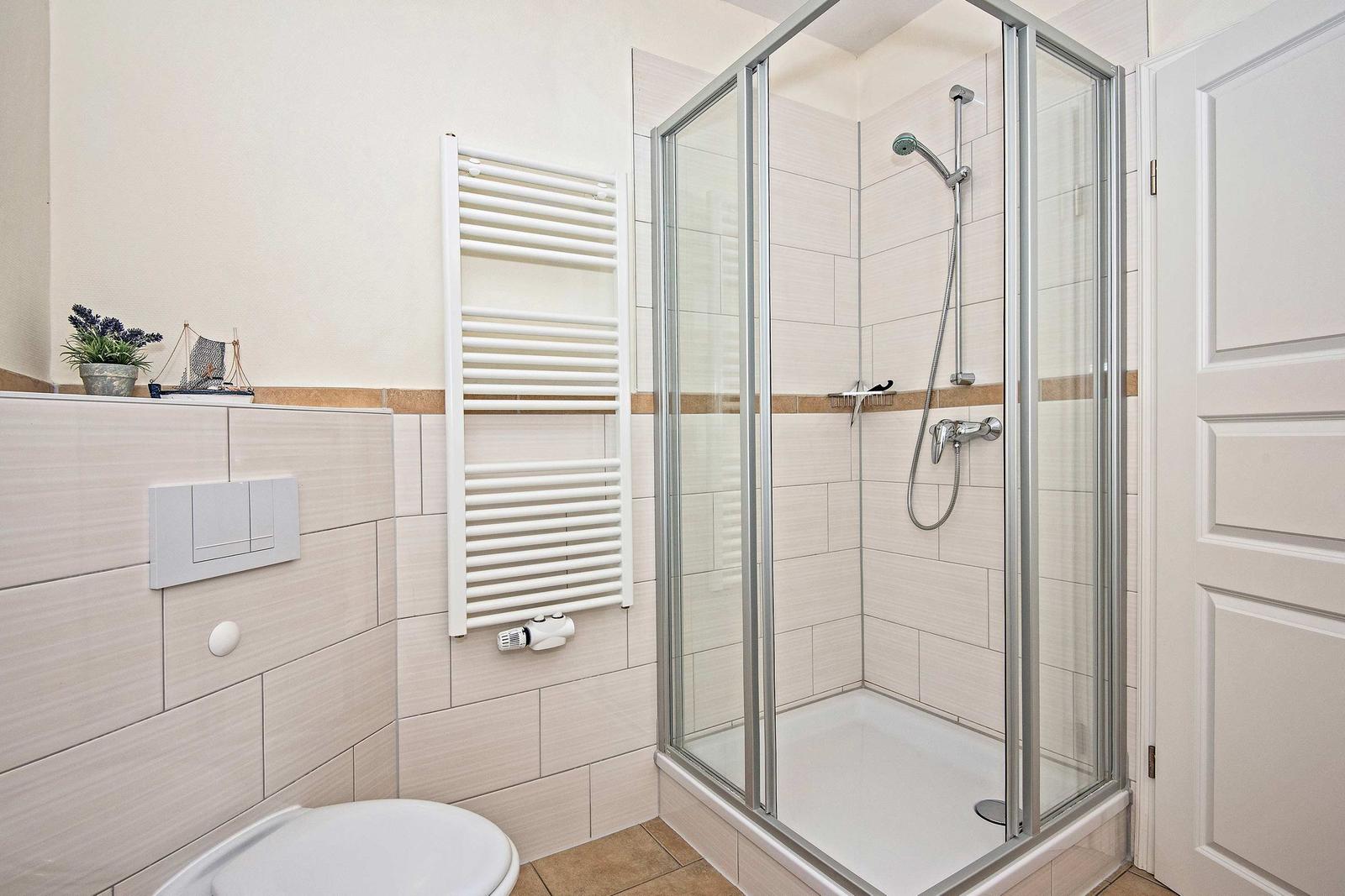 Bad mit Dusche, Heizkörper und Toilette. Wandverkleidung und Bodenfliesen.