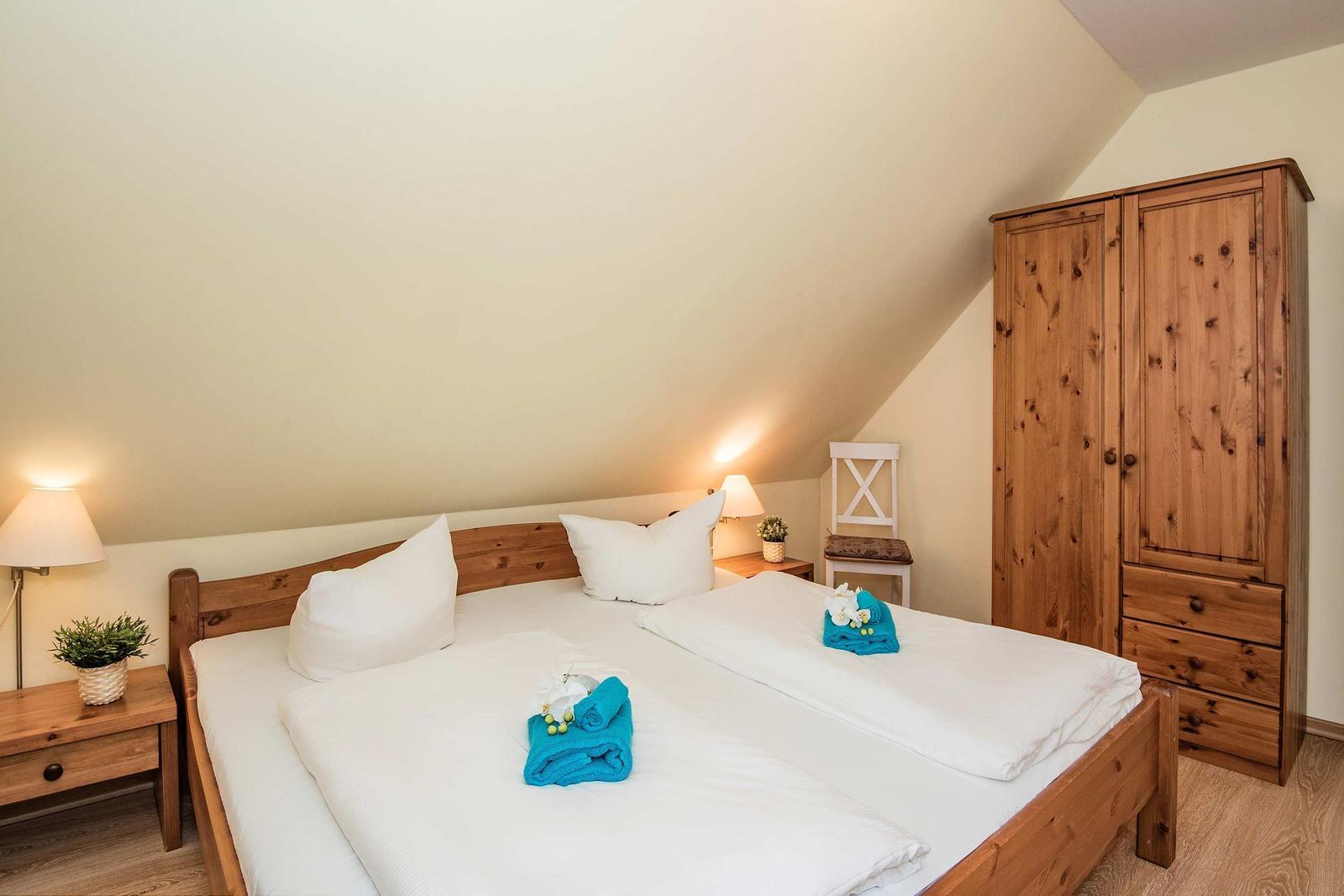 Schlafzimmer mit Doppelbett, Holzmöbel und Schranksystem unter Dachschräge.