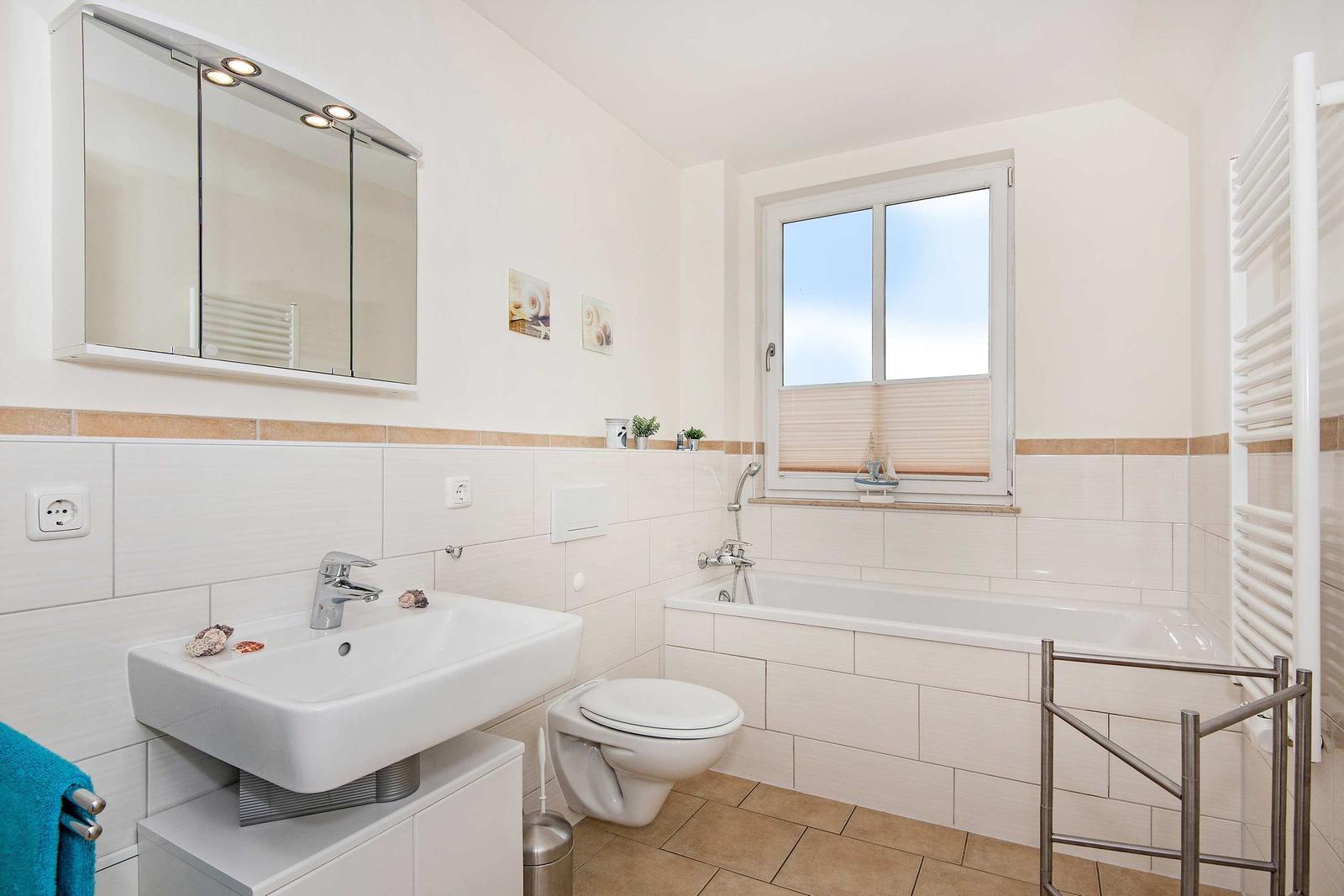 Badezimmer mit Badewanne, Waschbecken und Toilette. Fenster mit Jalousie und Heizkörper.
