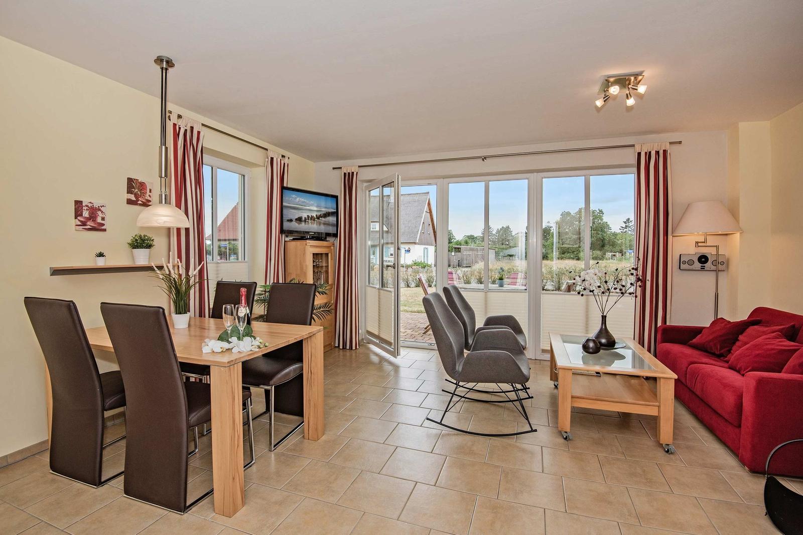 Wohn- und Essbereich mit rotem Sofa, Esstisch und Glasfront zur Außenterrasse.