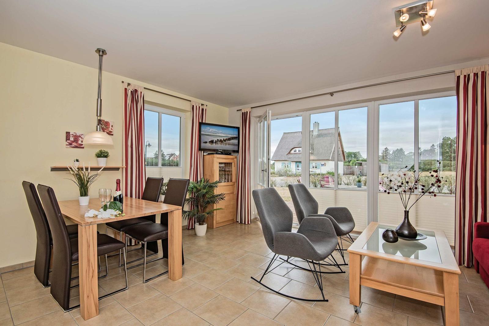 Wohn- und Essbereich mit Sitzgruppe, Esstisch und TV. Große Fenster mit Blick nach außen.