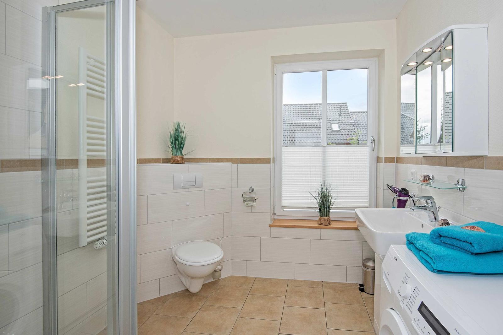 Badezimmer mit Dusche, Toilette, Waschbecken und Fenster.