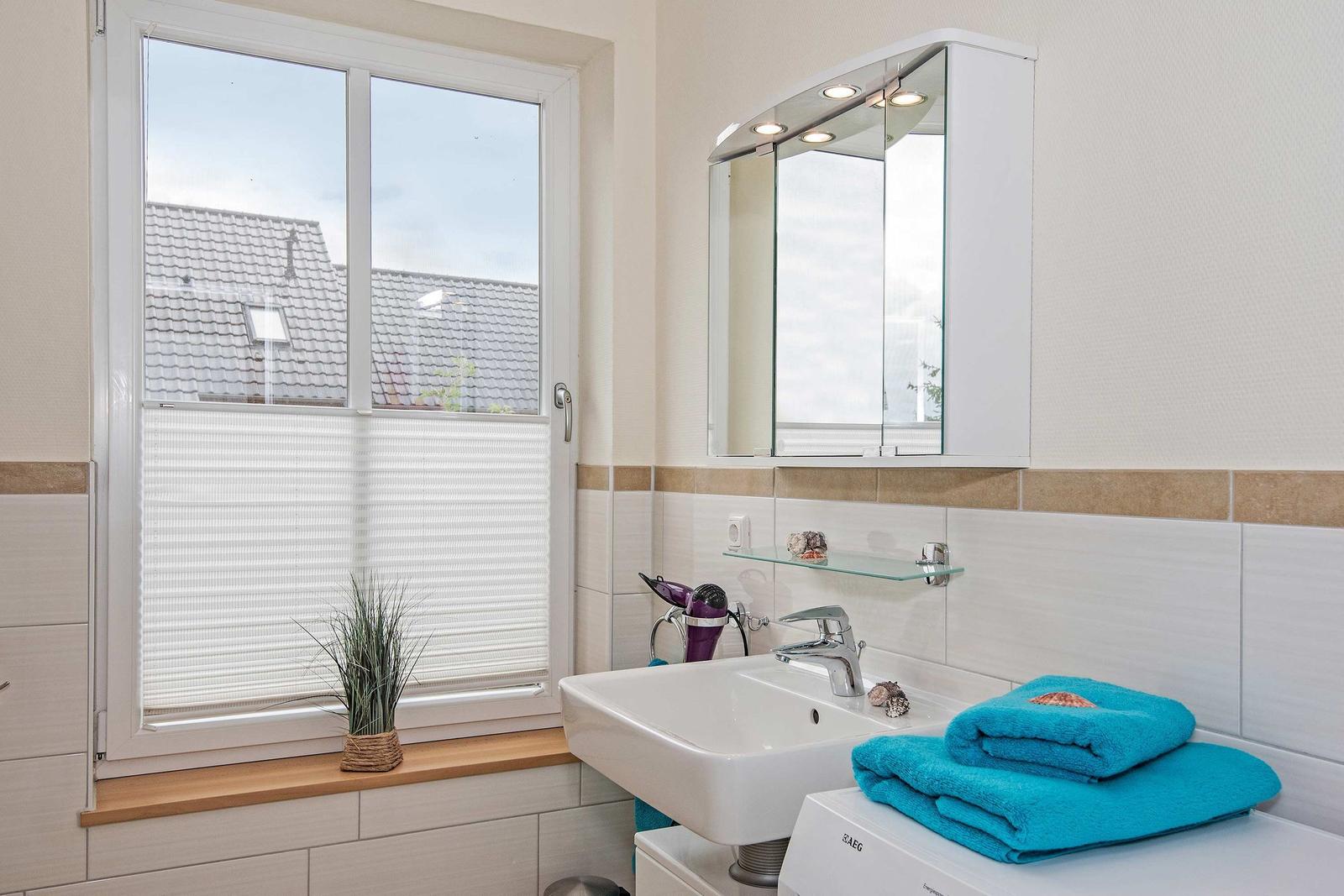 Badezimmer mit Waschbecken, Spiegelschrank und Fenster mit Jalousie.