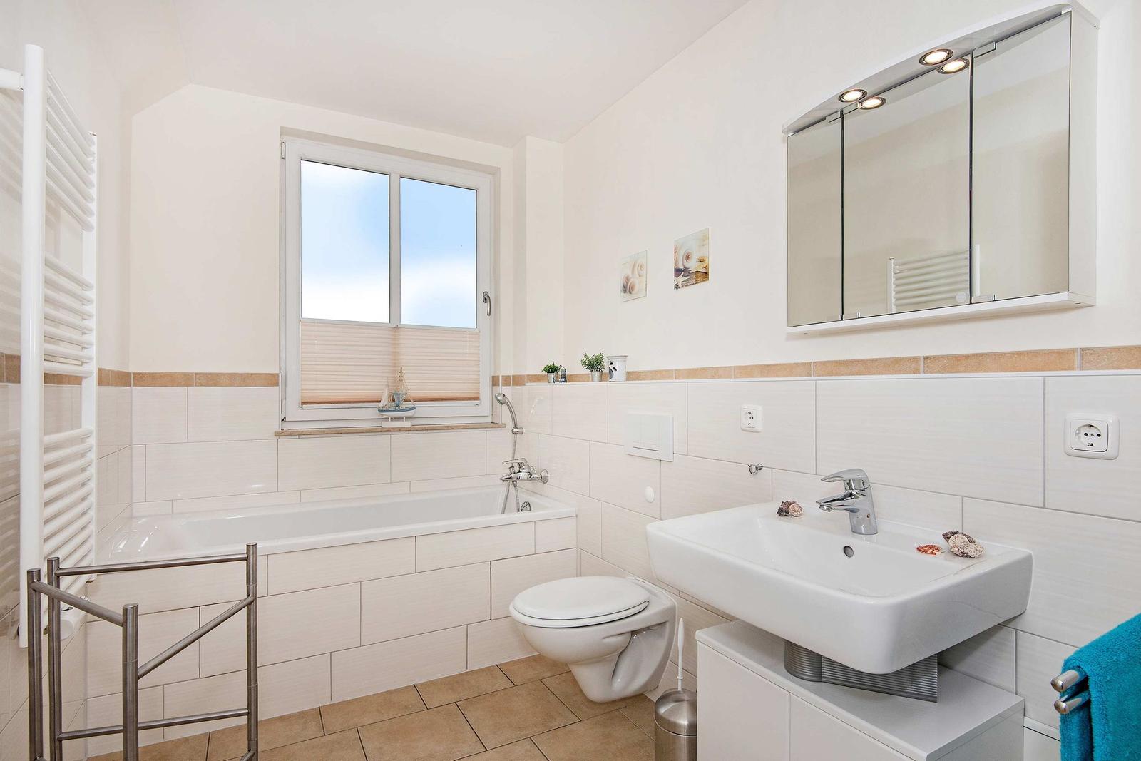 Badezimmer mit Badewanne, Waschbecken und Toilette. Fenster mit Jalousie und Spiegel über Waschbecken.