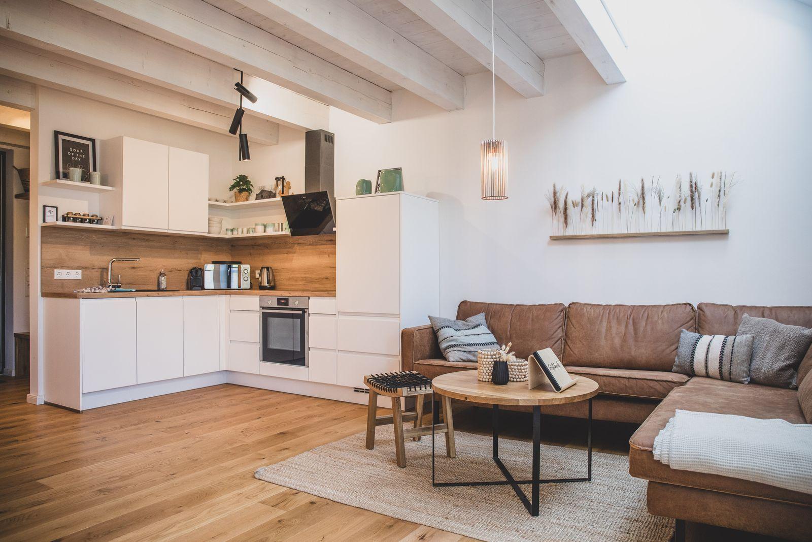 Wohnbereich mit Küchenzeile, braunem Sofa und Holzboden.