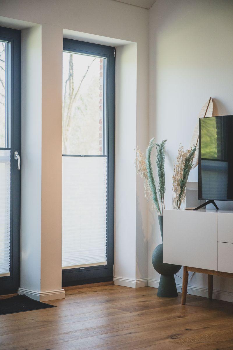 Ein Raum mit Holzboden, Fenster mit Jalousien und einem weißen Sideboard mit Pflanzen.