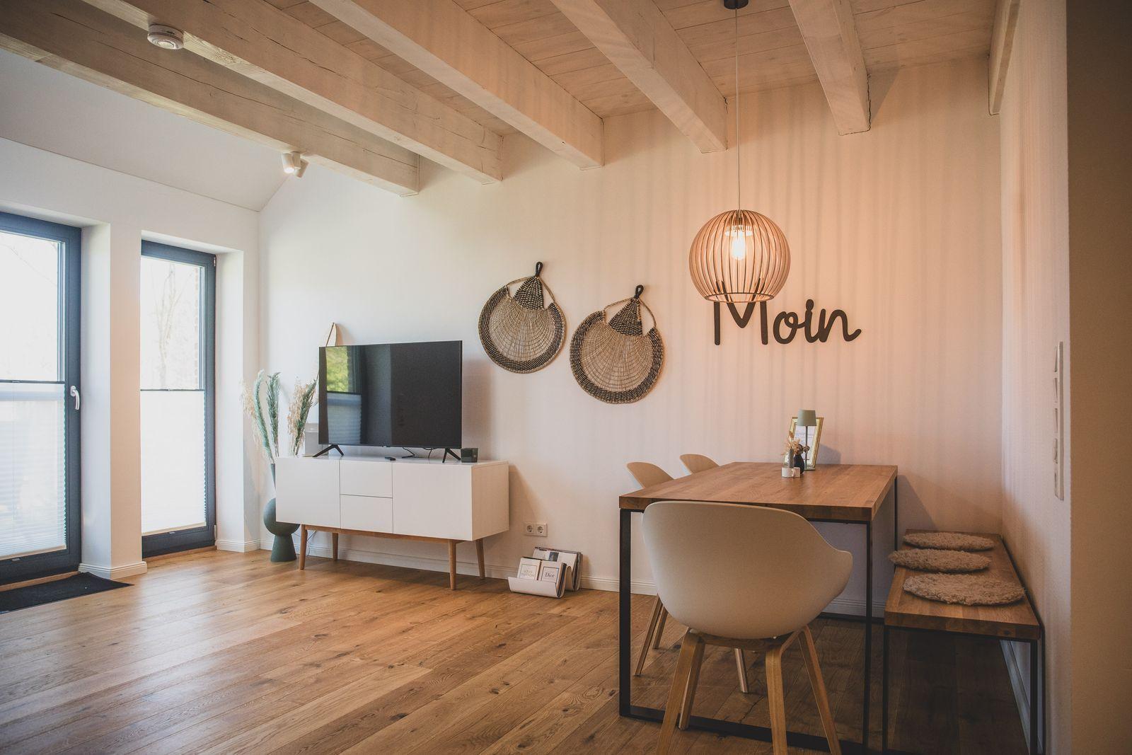 Wohn- und Essbereich mit Holzboden, TV, Tisch und Stühlen sowie Wanddekoration.