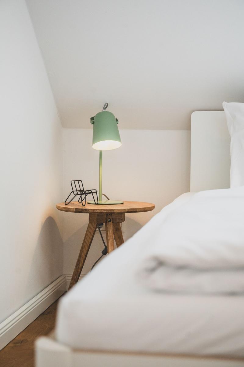 Schlafzimmer mit weißem Bett, Holztisch und grüner Lampe
