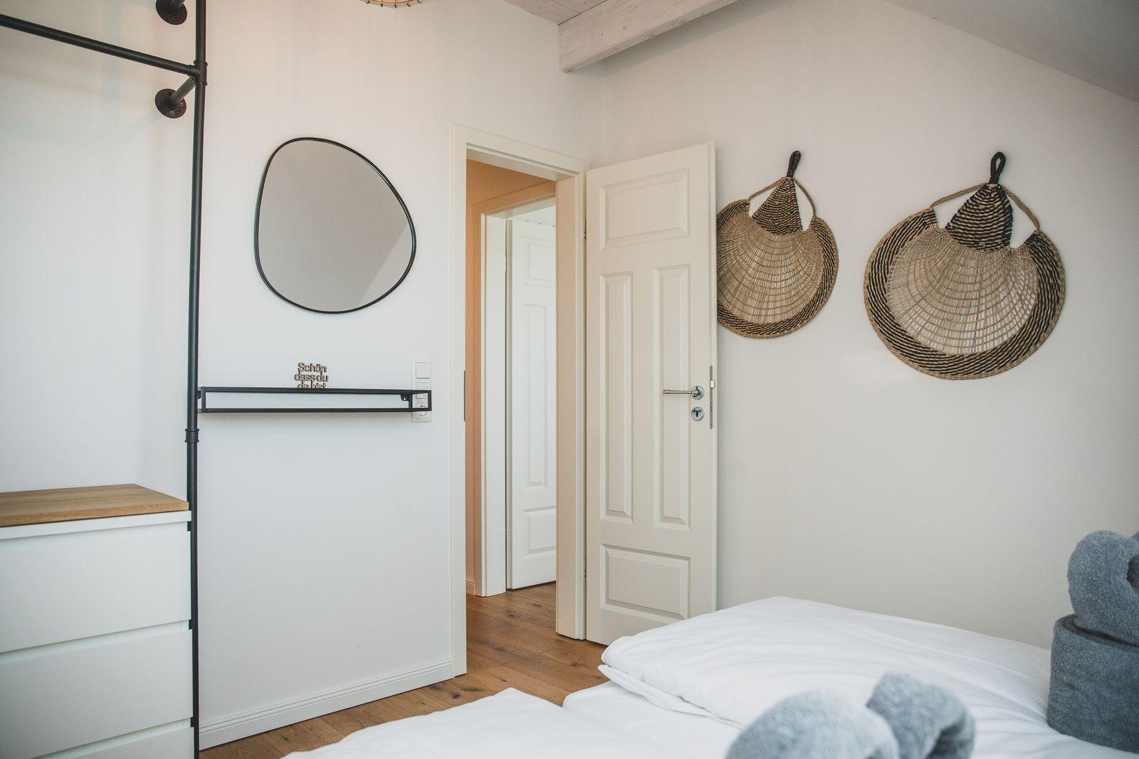 Schlafzimmer mit weißem Bett, Wandspiegel und zwei Wandkörben.