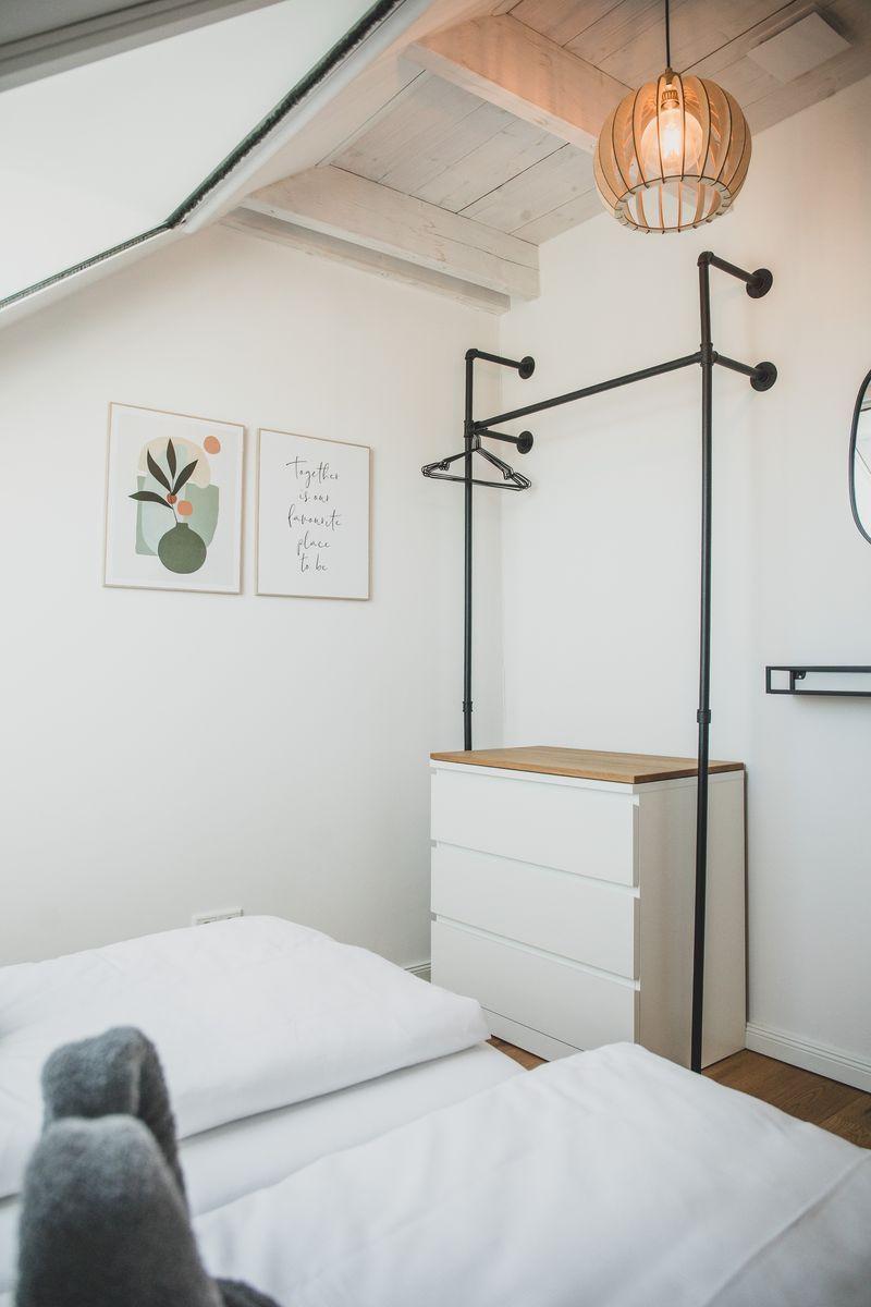 Schlafzimmer mit Bett, Kleiderständer und Deckenlicht. Wandbilder und Holzboden.