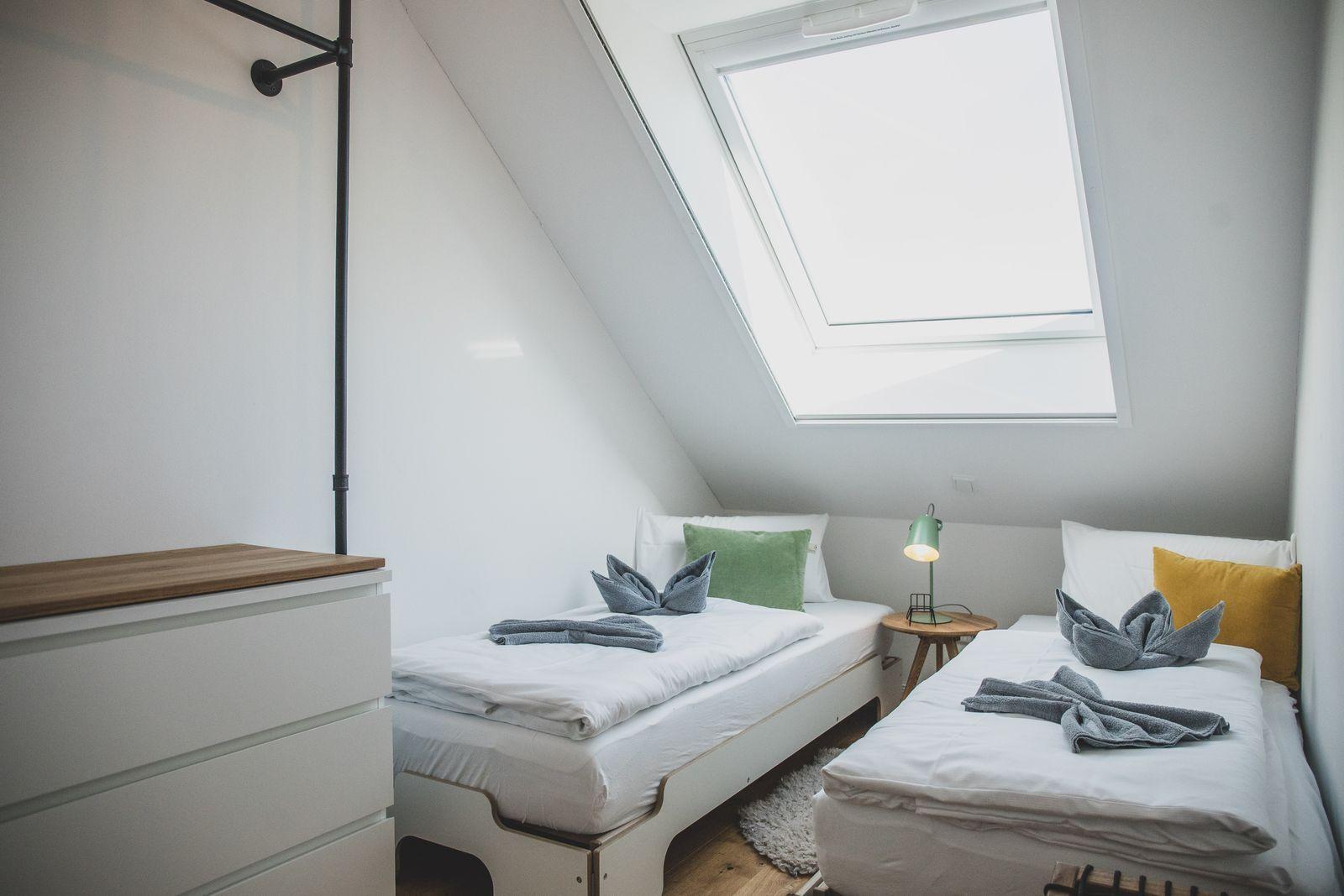 Zwei Einzelbetten unter Dachschrägen mit Dachfenster und Nachttisch.