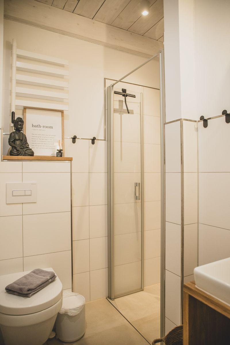 Badezimmer mit Dusche, Toilette und Waschbecken. Holzdecke und weiße Fliesen.