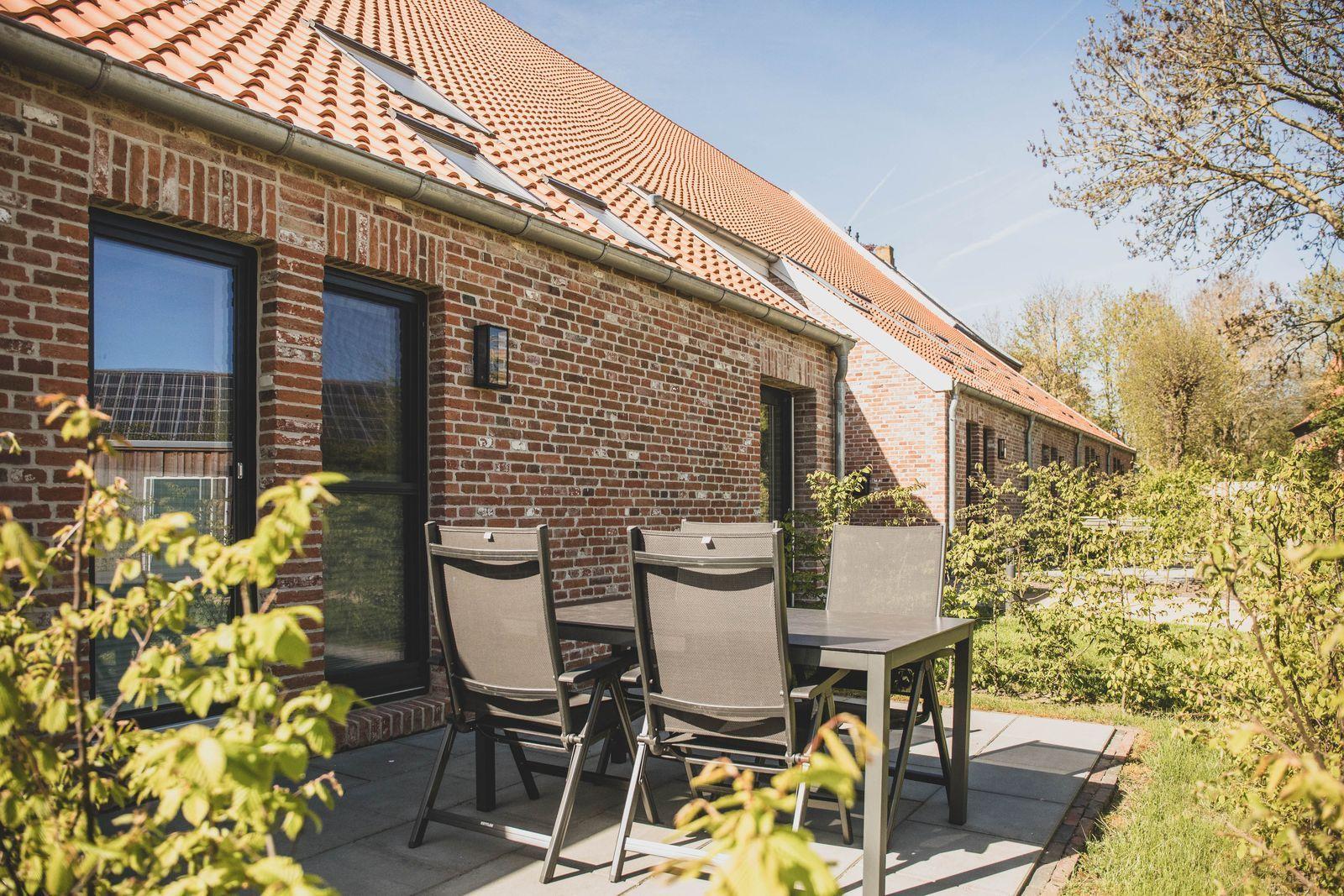 Terrasse mit Tisch und Stühlen vor einem Backsteinhaus mit rotem Dach.