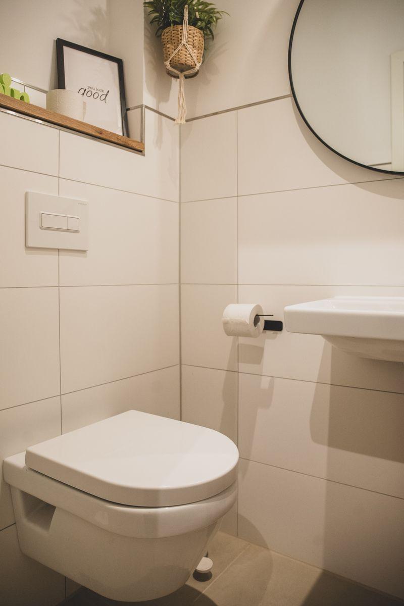 Badezimmer mit Toilette, Waschbecken und Spiegel. Wandhalterung für Toilettenpapier.
