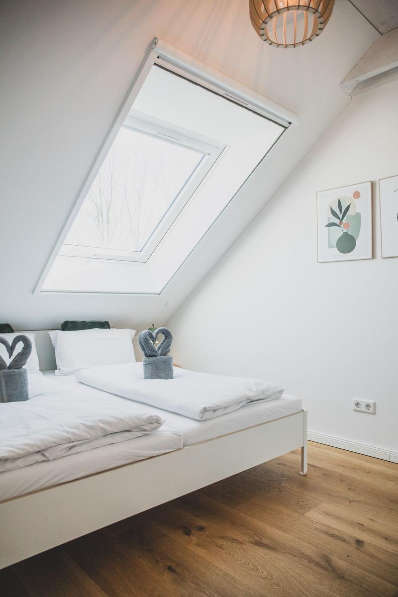 Schlafzimmer mit Dachfenster, Bett und Holzboden. Wandbilder und Lampe sind sichtbar.