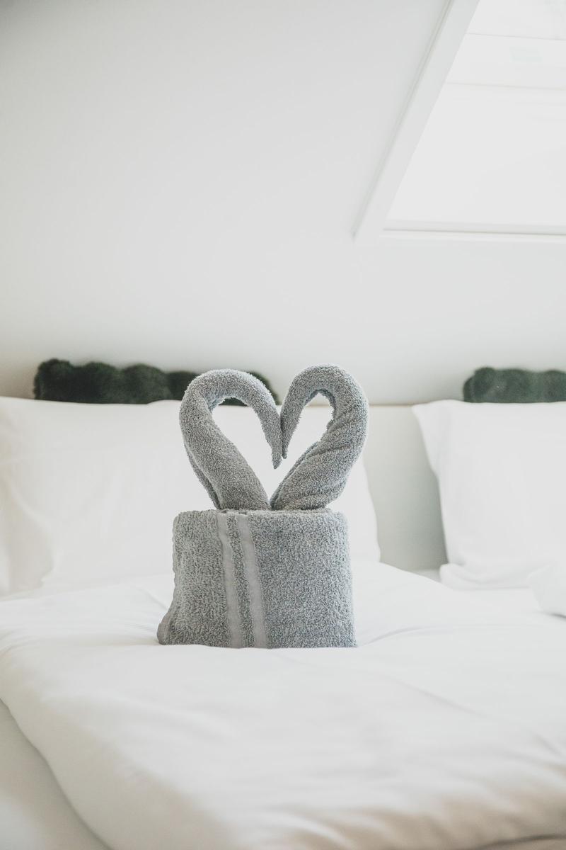 Zwei Handtücher sind als Schwäne geformt und bilden ein Herz auf dem Bett.