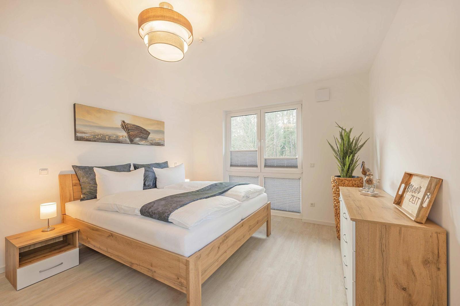 Schlafzimmer mit Holzbett, Nachttisch und Schrank. Fenster mit Jalousie und Wandbild.