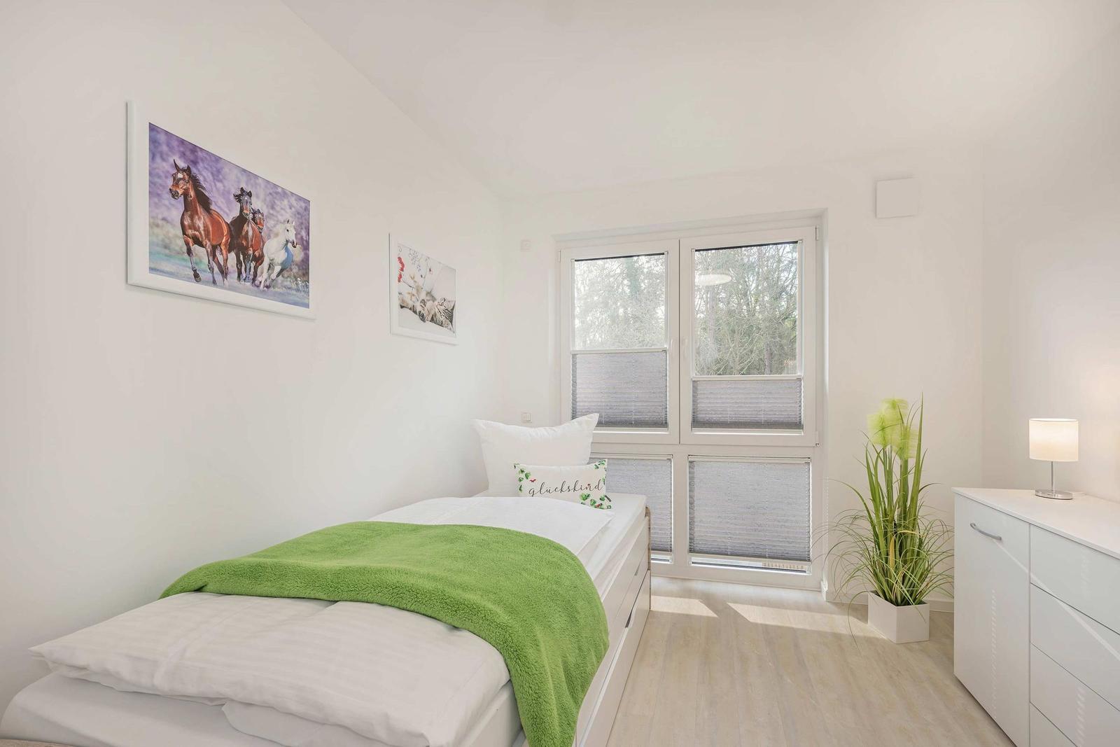 Ein Schlafzimmer mit Bett, Fenster und Schrank. An der Wand hängen Bilder.