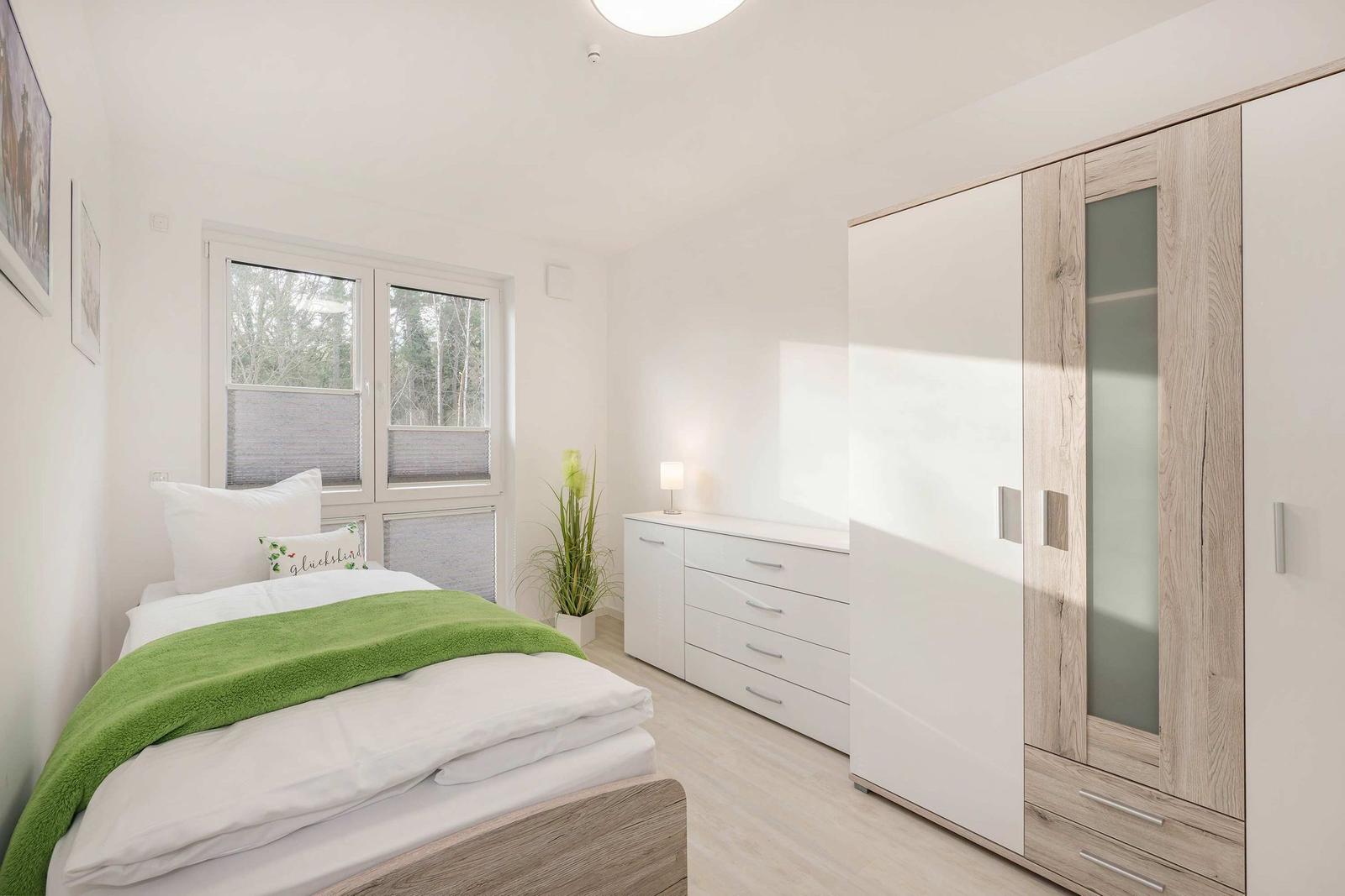 Schlafzimmer mit Bett, Kleiderschrank und Fenster zum Wald.