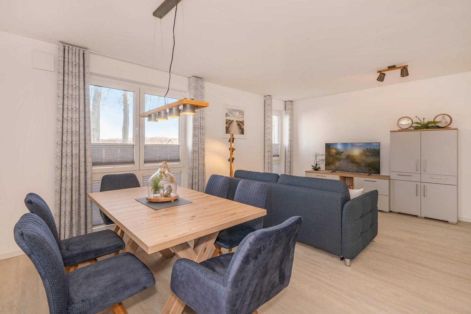 Essbereich mit Holztisch und blauen Stühlen. Wohnbereich mit Sofa und Fernseher.