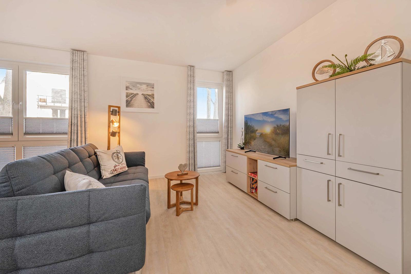 Wohnzimmer mit Sofa, Fernseher und Kleiderschrank. Holzfußboden und Fenster mit Jalousien.