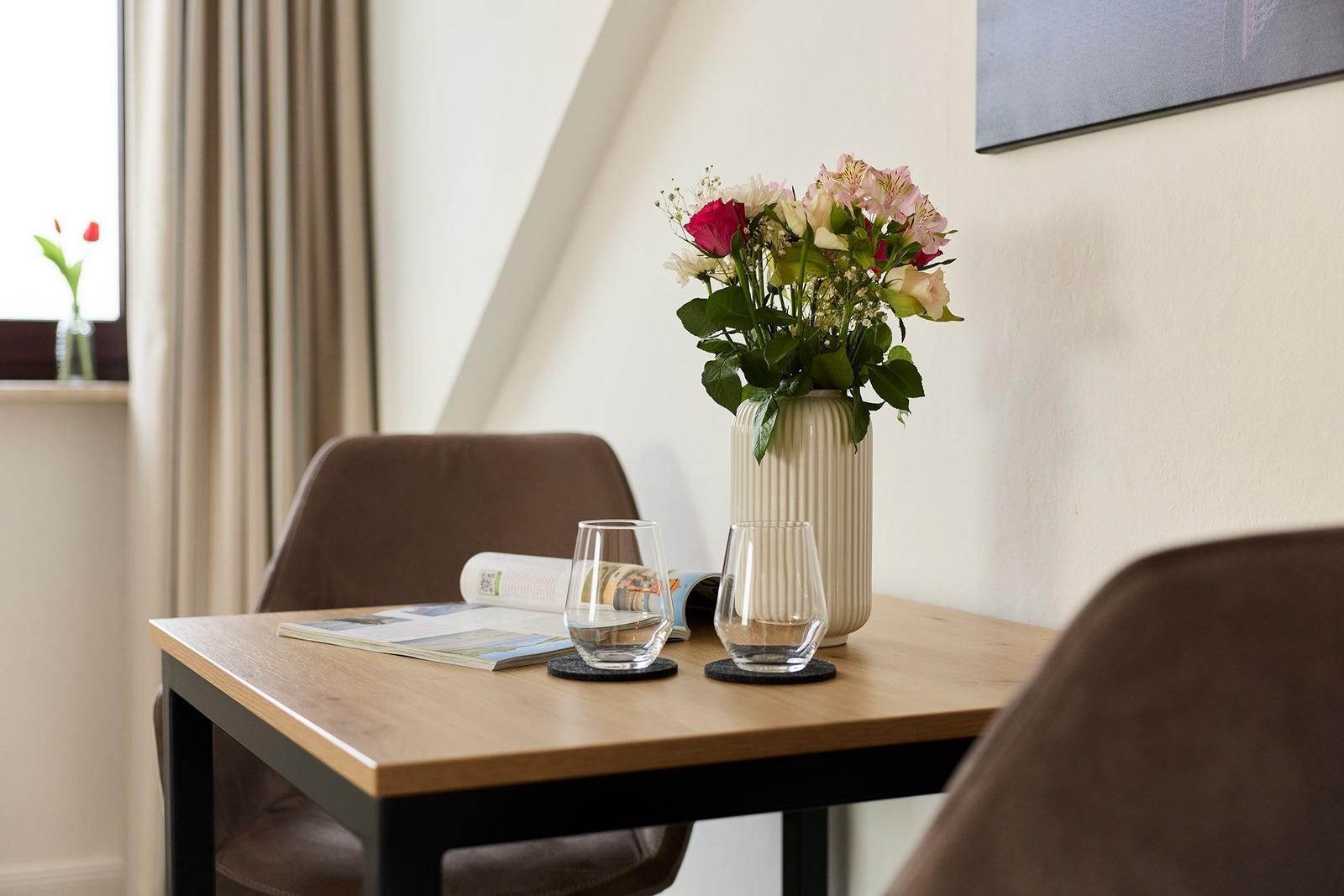 Ein Tisch mit zwei Gläsern, einer Blumenvase und einer Zeitung.