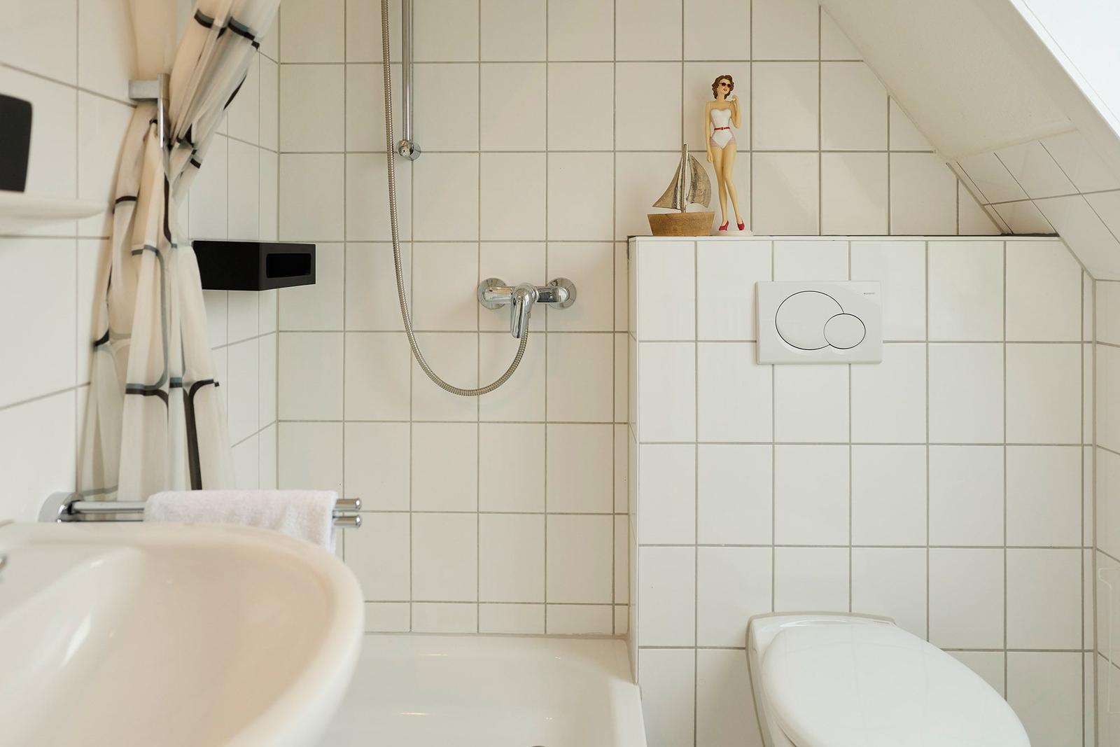 Badezimmer mit Dusche, Waschbecken und Toilette. Auf dem WC-Deckel steht eine Figur.