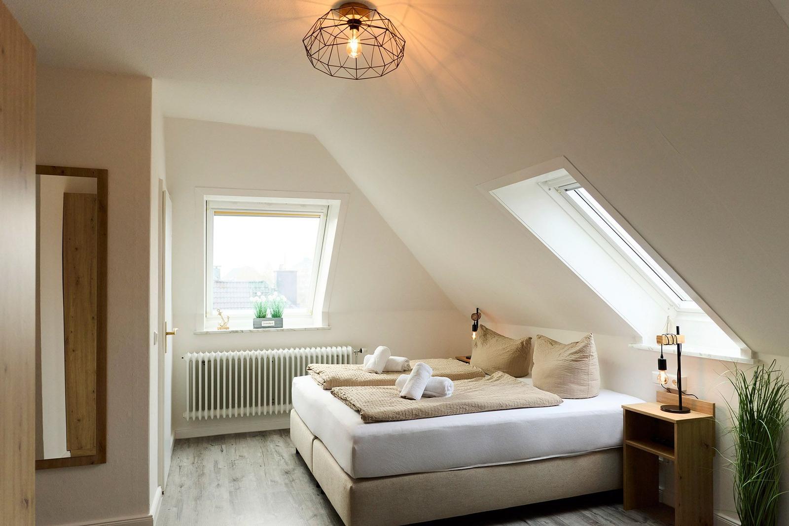 Schlafzimmer mit Dachschrägen, Bett, Nachttisch und Fenster.