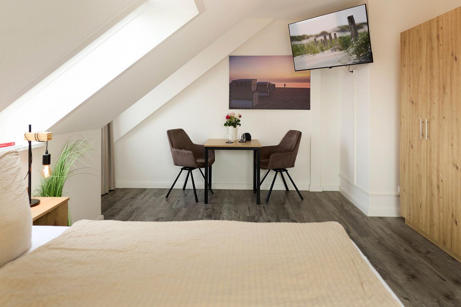 Ein Schlafzimmer mit Dachschrägen, einem Tisch mit zwei Stühlen, einem Fernseher und einem Kleiderschrank.