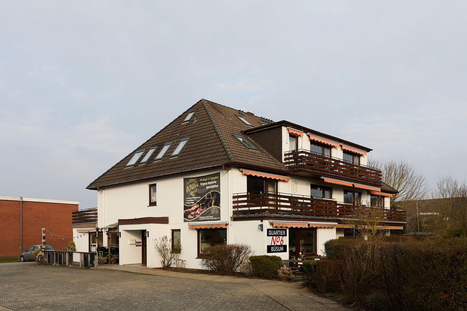 Ein zweistöckiges Haus mit Balkonen und Satteldach. An der Fassade hängt ein Werbeplakat.