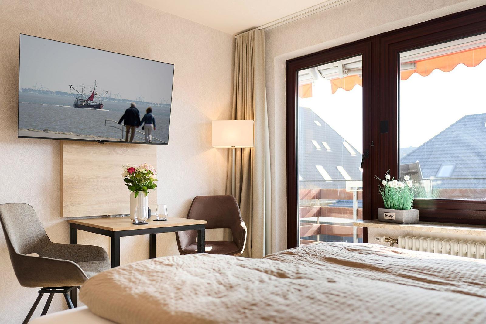 Zimmer mit Bett, Fernseher und Blick auf Balkon.