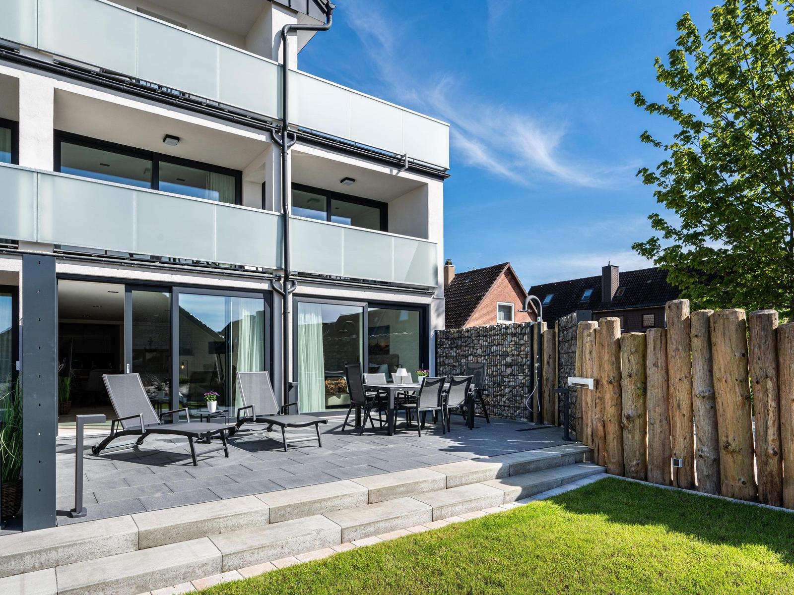 Terrasse mit Liegen und Tisch, moderne Villa mit Glasbrüstungen und Holzzaun.