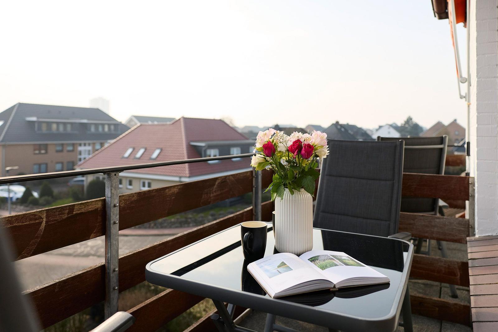 Terrasse mit Tisch, Stühlen, Blumen und offenem Buch.