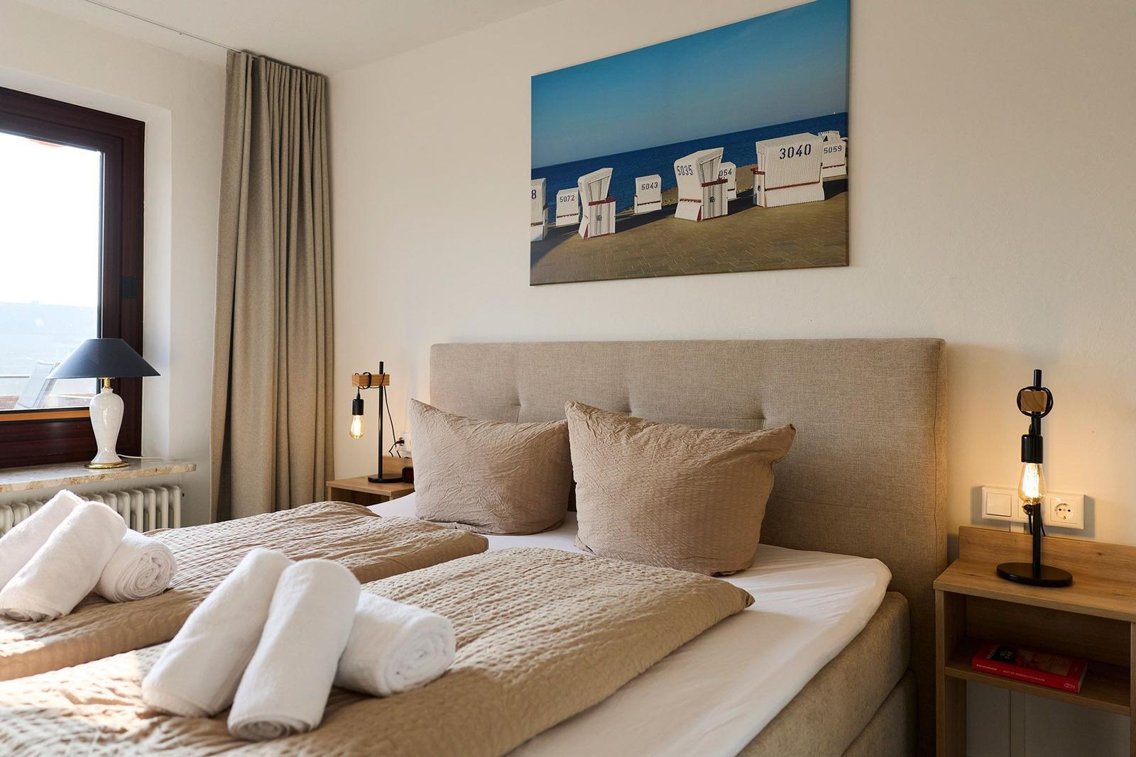 Schlafzimmer mit Bett, Nachttischen und Wandbild von Strandkörben.