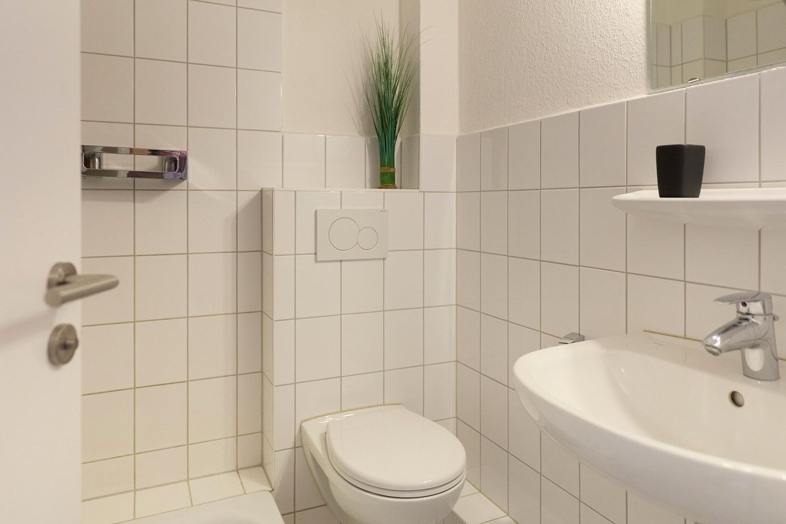 Badezimmer mit Toilette, Waschbecken und Spiegel. Wandverkleidung aus weißen Fliesen.