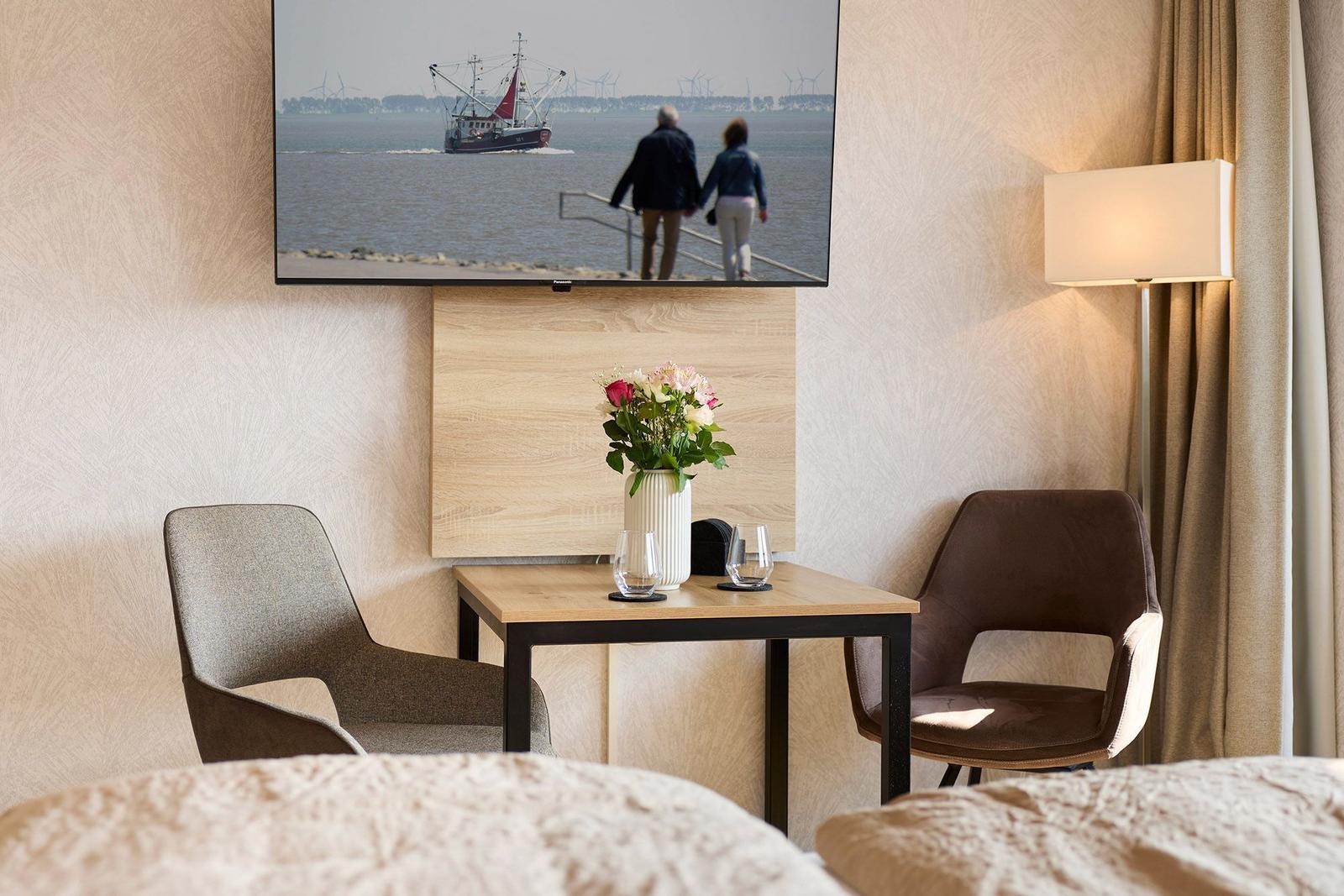 Zimmer mit Tisch, zwei Stühlen und Fernseher an der Wand.