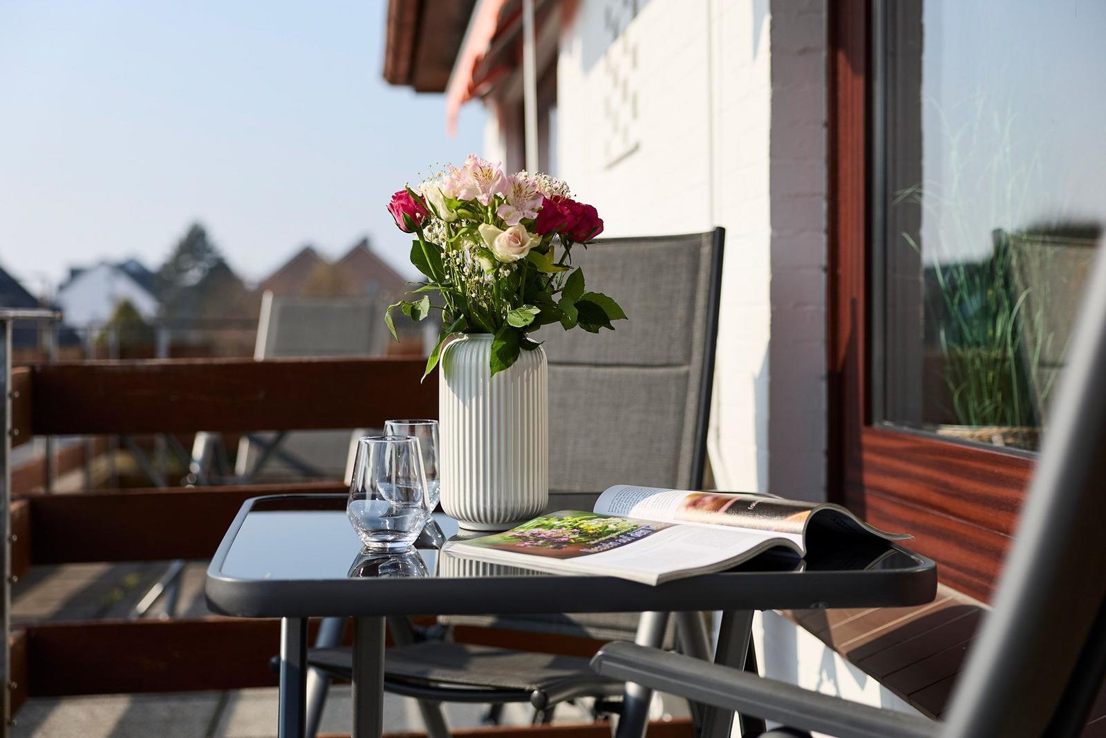 Terrasse mit Tisch, Stühlen, Blumen und offenem Buch.
