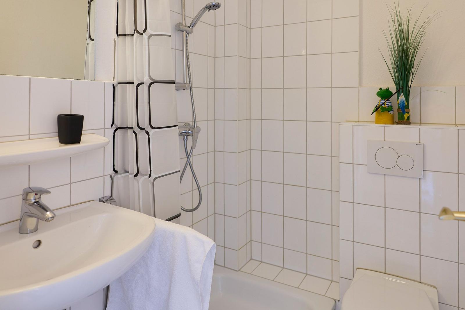 Badezimmer mit Dusche, Waschbecken und Toilette. Weiße Fliesen und schwarze Duschvorhang.