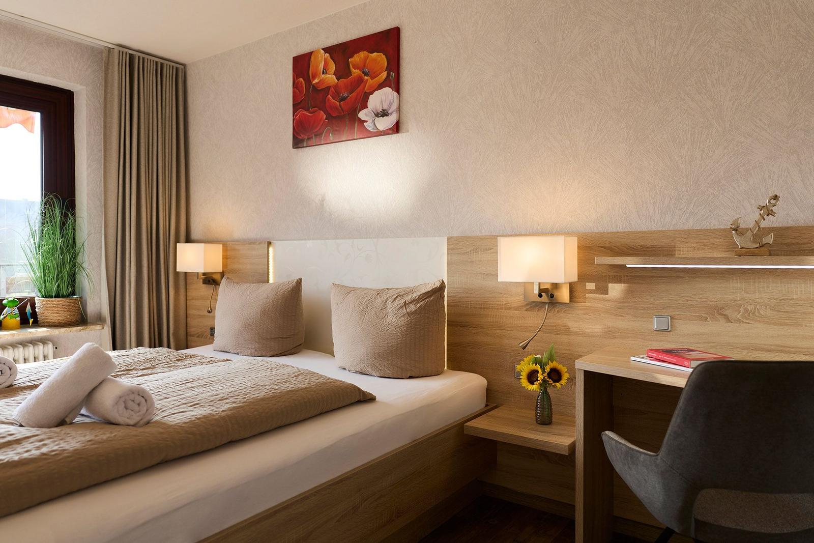 Ein Schlafzimmer mit Bett, Schreibtisch und Wandbild mit Blumen.