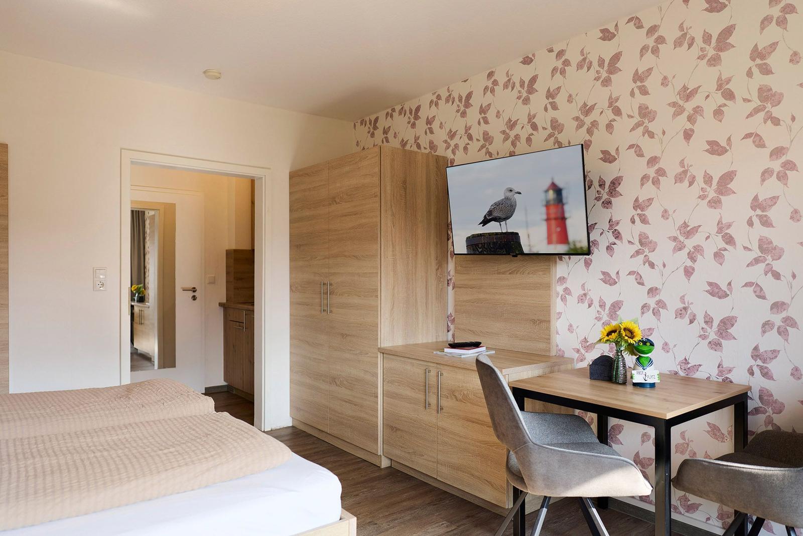 Schlafzimmer mit Bett, Schreibtisch und Fernseher an der Wand mit Blumenmotiv.