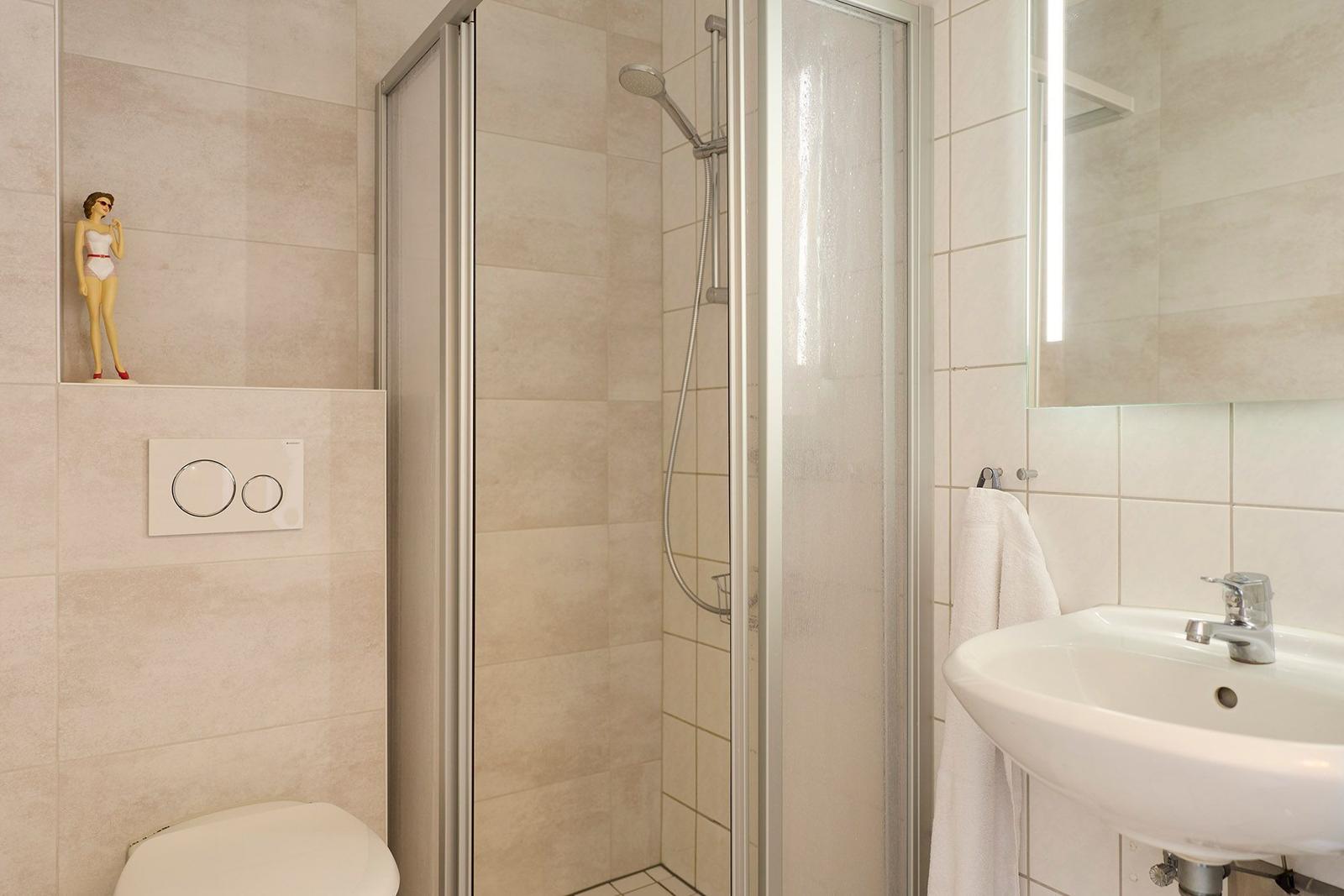 Bad mit Dusche, Waschbecken und Toilette. Eine Figur steht auf der Wand.