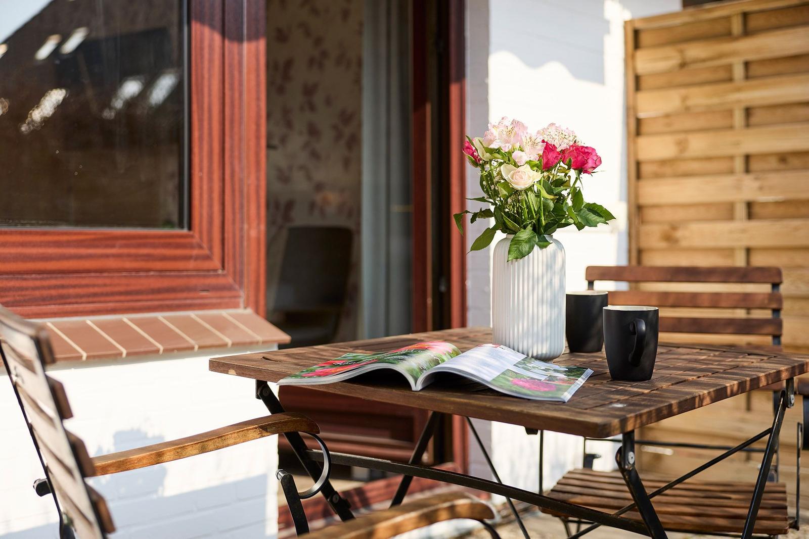 Terrasse mit Holztisch, Stühlen, Blumen und Zeitschrift.