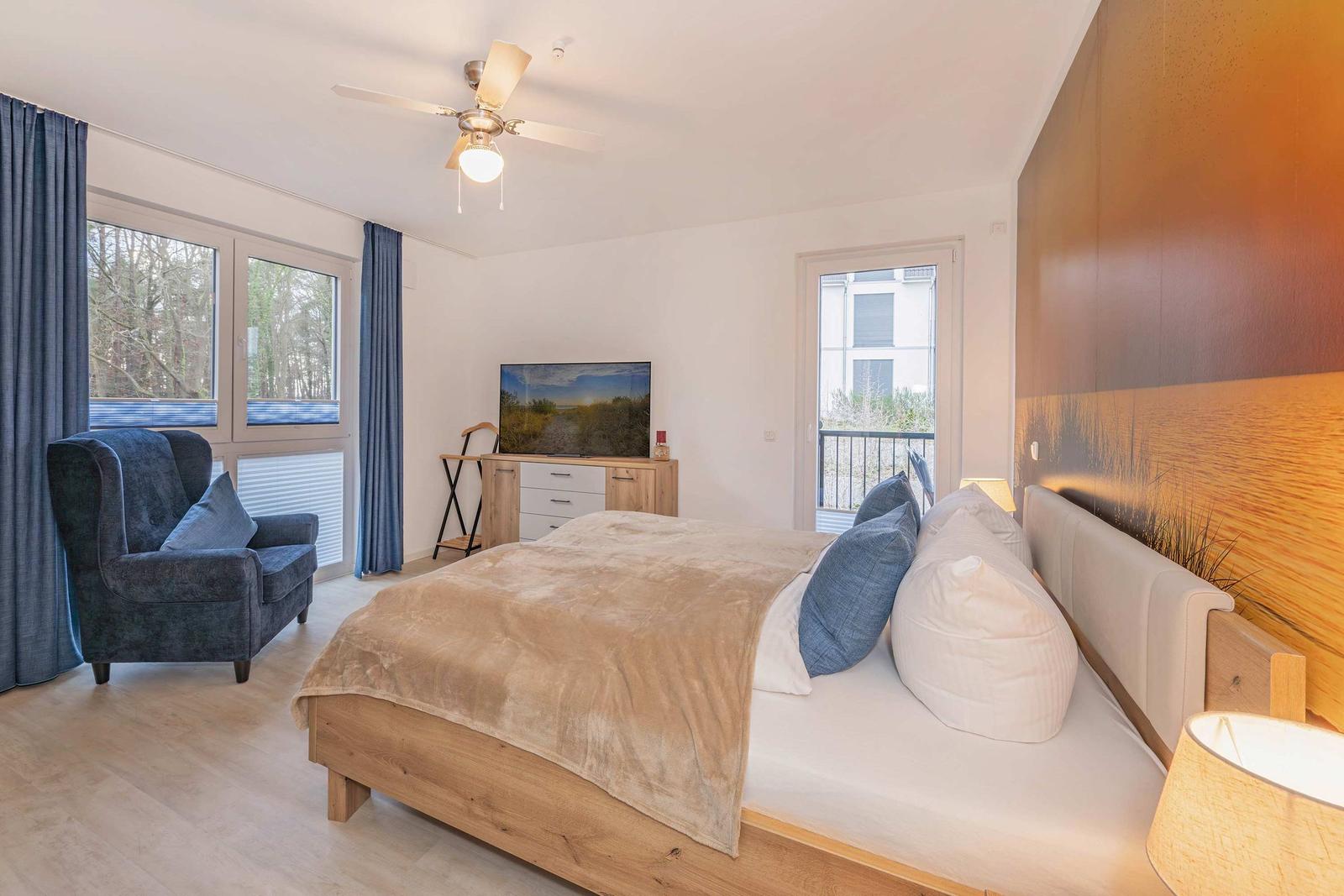 Schlafzimmer mit Bett, Fernseher und Sessel. Fenster und Balkontür.
