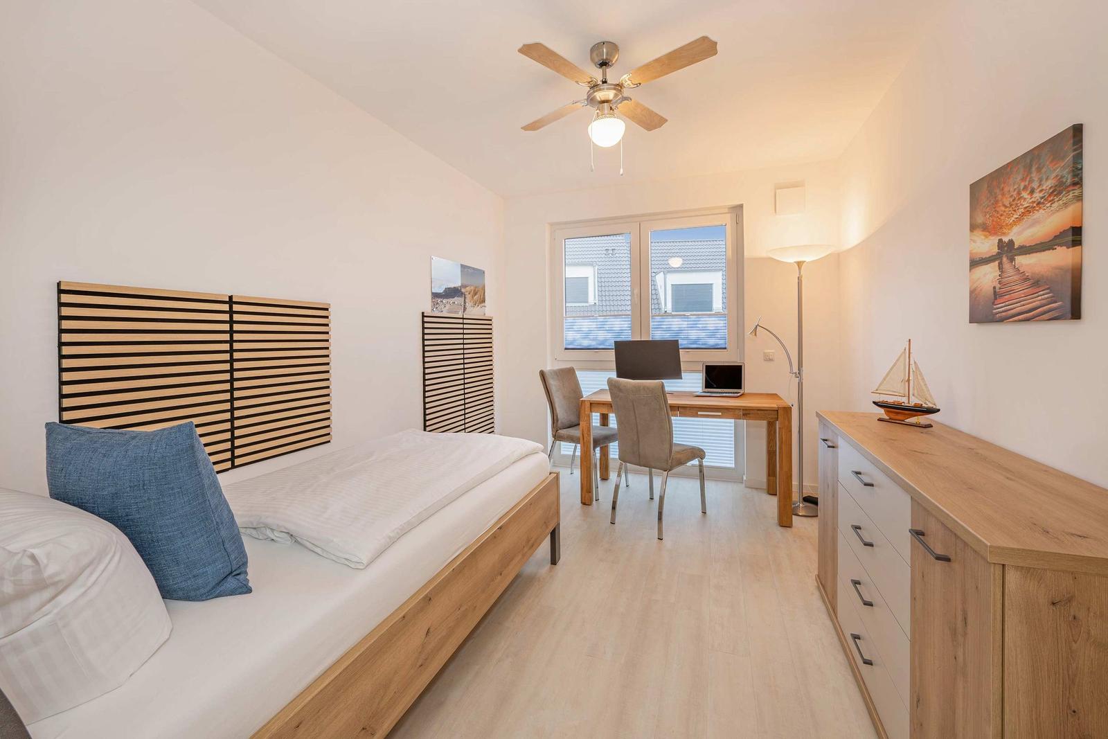 Schlafzimmer mit Bett, Schreibtisch und Fenster. Holzmöbel und Wandbild.