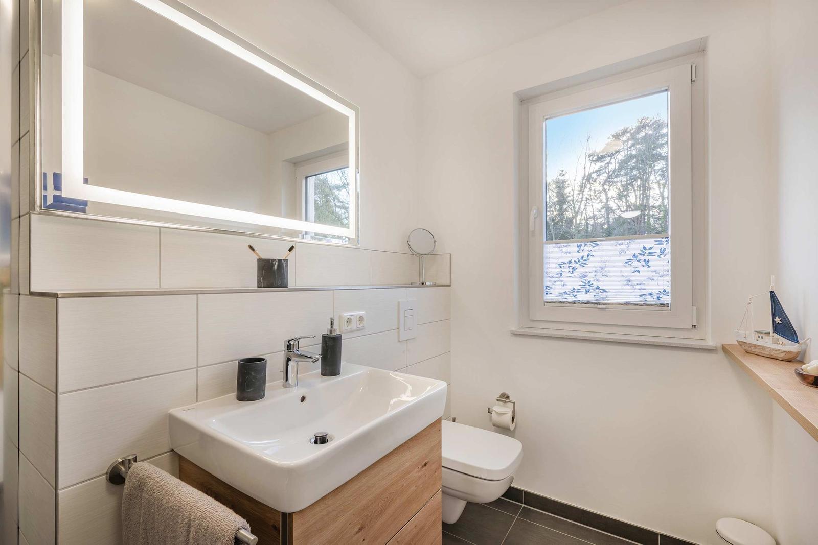 Badezimmer mit Waschbecken, Toilette und Fenster mit Blick auf Bäume.