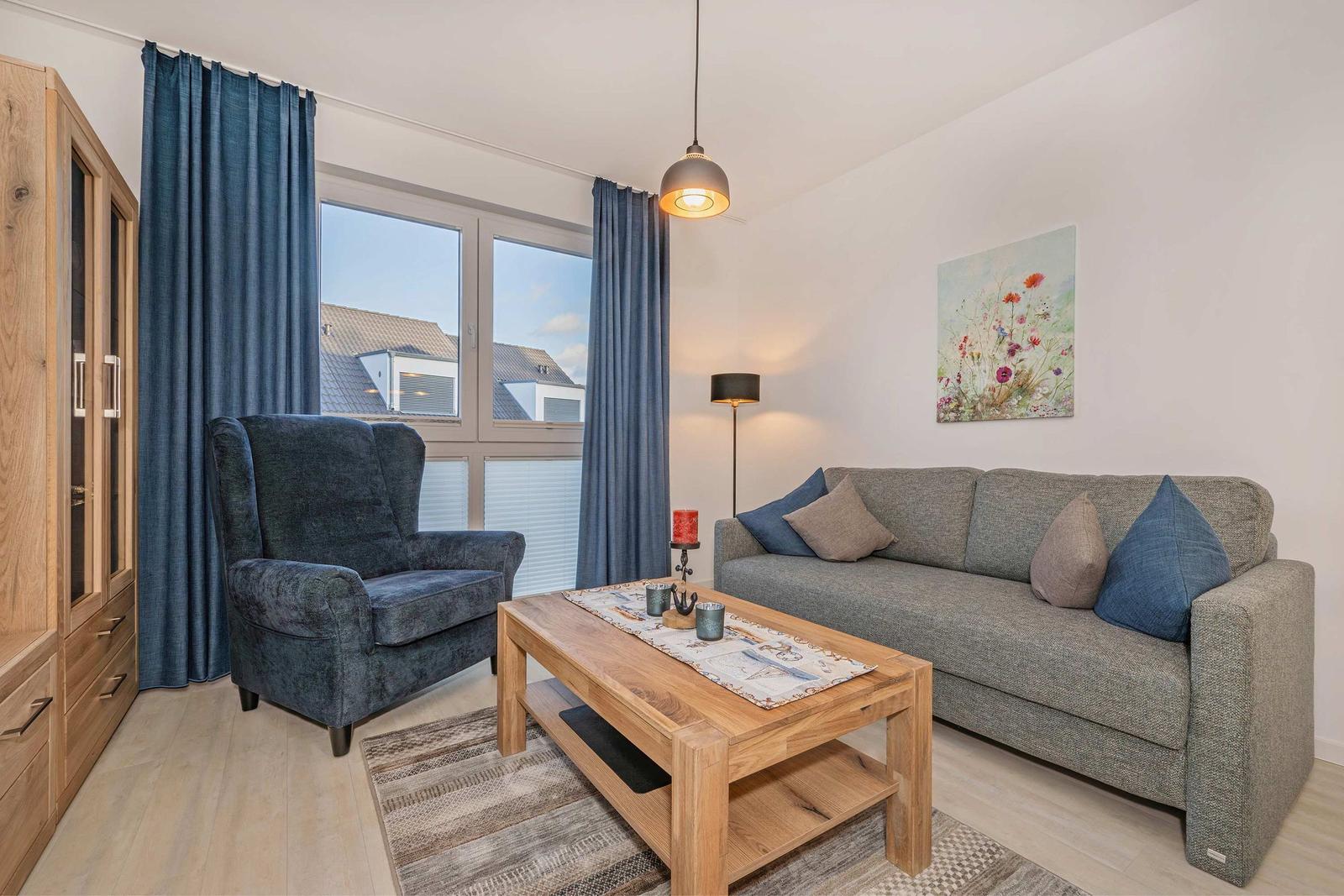 Wohnzimmer mit Sofa, Sessel, Holztisch und Fenster mit Blick auf Dächer.
